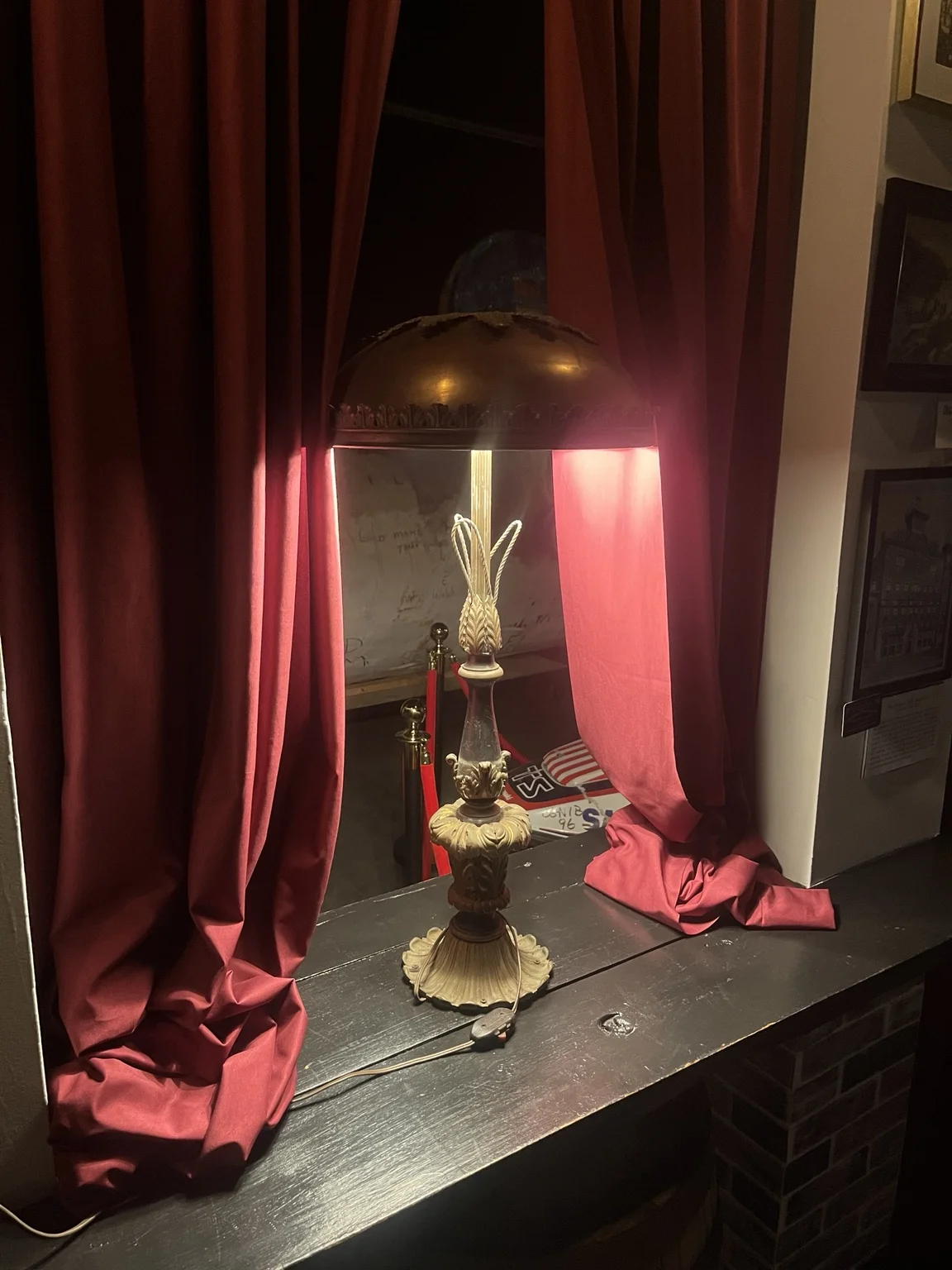 A small display beneath a lamp, set between burgundy curtains